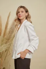 Chaqueta de satén color blanco, con diseño abierto sin botones, cuello mao y mangas largas con puños rectos.