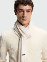 Bufanda de punto Raschel color blanco hueso, con diseño liso y terminación en flecos cortos. Incluye una pequeña etiqueta metálica con el logo de la marca.