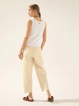 Pantalón color crema de tiro alto, tipo bombe, con recortes verticales en el delantero, pliegues en la bota con broche níquel, cintura con gancho pantalonero y botón interno, bolsillos ojal y pinza de entalle en la espalda.