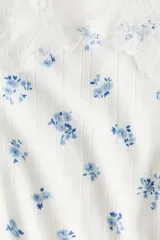 Top blanco de breteles finos en tejido pointelle con delicado estampado floral azul, escote recto con ribete de encaje y laterales fruncidos.