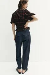 Pantalón chino de tiro medio confeccionado en denim oscuro. Presenta pinzas en el delantero, bolsillos laterales y bajo con acabado en vuelta. Cierre frontal con cremallera y botón.