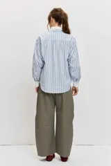 Camisa de rayas celestes y marrones, de corte holgado y manga larga, con cuello en V y detalles blancos en el cuello y los puños.