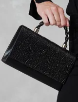 Cartera de mano negra con strass, asa trenzada y asa secundaria de cadena metálica removible. Cierre con botón imantado y bolsillo interior.