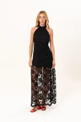 Vestido largo de encaje negro con cuello halter, compuesto por un minivestido base y una sobrefalda transparente de encaje con diseño floral.