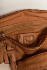 Cartera de cuero color negro con efecto lavado y desgastado, estilo vintage. Cuenta con múltiples bolsillos con cierre delantero, tiras colgantes y doble asa corta de mano.