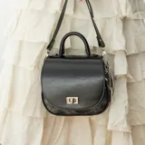 Cartera bandolera de cuero color marrón con asa corta superior y correa larga ajustable.