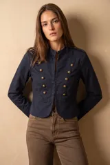 Chaqueta corta color beige de algodón, de inspiración militar con cuello mao y doble botonadura frontal con botones metálicos dorados.