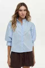 Camisa blanca de cuello mao con volados, mangas abullonadas y cierre frontal con botones.