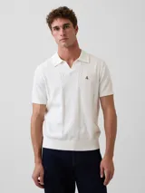 Buzo tipo polo color blanco óptico, de manga corta, tejido de punto con detalles de calados verticales en el frente y pequeño bordado alusivo en el pecho.