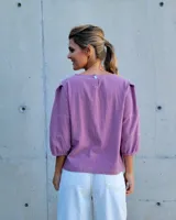 Blusa de mangas tres cuartos con diseño de corte recto y cuello redondo. Presenta costuras horizontales decorativas en las mangas y un acabado liso.