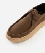 Championes de estilo casual con diseño moc toe, confeccionadas en cuero gamuza color marrón. Presentan costura visible en la puntera, cierre con cordones y suela de goma en tono beige de perfil bajo.