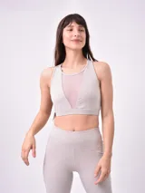 Top deportivo de color taupe con diseño de cuello redondo y panel central de malla transparente. Presenta un corte ajustado con banda elástica inferior para mayor soporte.