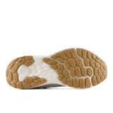 Championes deportivos New Balance modelo Arishi V4, con tecnología de amortiguación Fresh Foam en la entresuela. Presentan un diseño en tonos blanco y beige con detalles en lila en el logo lateral y la lengüeta, y suela de goma color caramelo.