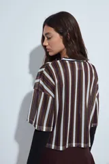 Remera de estilo deportivo con cuello en V y mangas cortas amplias. Presenta un diseño de rayas verticales en tonos marrones, blancos y líneas finas en fucsia, confeccionada en tejido de red.