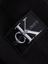 Sweater de punto negro con cuello alto y cierre frontal de cremallera. Presenta un pequeño parche con el logo 'ck' en la manga izquierda.