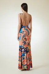 Vestido largo de corte al cuerpo con escote en V y breteles dobles finos. Presenta un estampado vibrante con motivos orientales, incluyendo aves y elementos florales en tonos naranja, azul y amarillo.