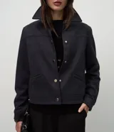 Chaqueta de corte recto confeccionada en suede sintético color marrón. Presenta cuello estilo camisa, cierre frontal con botones metálicos, mangas largas con puños ajustados y bolsillos embutidos.