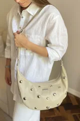 Cartera bandolera de cuero negro con diseño de media luna, decorada con tachas metálicas plateadas. Cuenta con correa regulable, cierre principal y bolsillo interior con forro.
