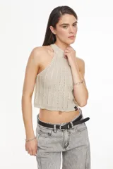 Top de punto estilo halter, color crudo, con cuello alto ajustado, diseño sin mangas y corte corto.