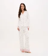 Pijama de dos piezas estilo americano, compuesto por camisa de manga larga con cuello en V, botones frontales y bolsillo en el pecho, y pantalón largo con cintura elástica. Presenta un estampado floral delicado sobre fondo blanco y detalles de encaje rosado en los puños y el ruedo del pantalón.