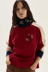 Sweater de tejido de punto con mangas raglan, cuerpo principal rojo, mangas color beige y puños y cuello en azul marino. Presenta un bordado central con un motivo de pájaro y espigas.