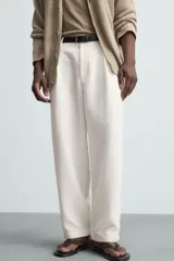 Pantalón blanco de corte relajado (relaxed fit) con pliegues frontales, bolsillos laterales y bolsillos traseros de vivo. Cierre frontal con cremallera y botón.