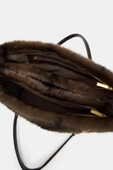 Bolso de hombro con cuerpo de textura efecto pelo en color marrón oscuro. Cuenta con un asa de hombro combinada con cadena metálica dorada, bolsillo exterior frontal y cierre principal mediante cremallera.