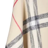 Poncho de tejido de punto con diseño de cuadros escoceses en tonos beige, negro y rojo. Presenta un corte amplio, cuello abierto y terminaciones con flecos en el ruedo.
