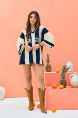 Remerón tejido de punto oversize, con diseño de rayas verticales en colores crudo y azul marino. Cuenta con escote en V y la palabra "BRASIL" estampada en el frente.