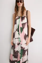Vestido midi de corte holgado con cuello halter ajustable mediante lazada y hombros descubiertos. Presenta un diseño con tiras cruzadas en la espalda y un estampado abstracto en tonos rosado, verde y marrón sobre fondo blanco.