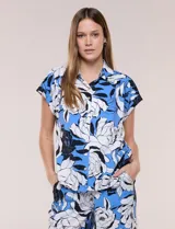 Camisa de manga corta confeccionada en rayón y poliéster, con estampado floral en tonos azules, negros y blancos, cuello camisero clásico y cierre frontal de botones.