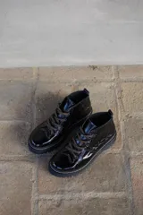 Borcegos de cuero charolado negro con cordones jaspeados en tonos marrones y suela track dentada con costura blanca visible.