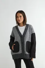 Saco tipo cardigan de punto gris con diseño híbrido. Presenta mangas largas y bolsillos frontales de tela técnica acolchada en color negro, con cierre frontal de botones y bordes acanalados.