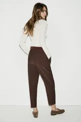 Pantalón de tiro alto en color beige, con diseño de pinzas frontales y bolsillos laterales. Incluye un cinturón a contraste en tono marrón con hebilla metálica y cierre frontal con cremallera y gancho.