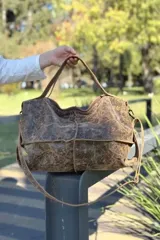 Bolso tipo shopper de cuero con acabado desgastado y textura rústica. Cuenta con doble correa de mano, correa larga ajustable y extraíble, cierre superior y costuras visibles que realzan su diseño artesanal.