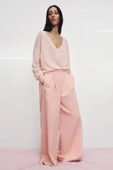 Pantalón de tiro medio con corte wide leg, confeccionado en algodón. Presenta cintura con trabillas, bolsillos laterales ocultos y detalle de pliegues en el delantero. Cierre frontal con cremallera, botón y ganchos metálicos.