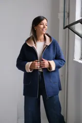 Tapado de paño azul marino con capucha, cierre frontal y detalles en color beige en el interior de la capucha, puños y bordes. Presenta bolsillos frontales aplicados y costuras visibles.
