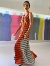 Vestido largo de lino rayado color naranja y marrón, con escote en V y espalda descubierta. La falda es amplia y con mucho movimiento.