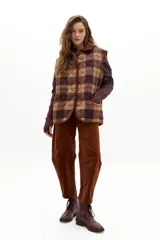 Chaleco acolchado de corte holgado con estampado de cuadros en tonos marrones y burdeos. Presenta cuello y ribetes en pana color caramelo, cierre frontal con botones a presión ocultos y bolsillos de parche delanteros.