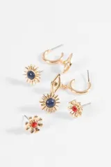 Set de tres pares de caravanas en tono dorado. Incluye un par de argollas con dije de ojo, un par de aros tipo sol con piedra central azul y un par de aros tipo flor con piedra central roja.