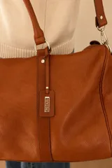 Bolso tipo Duffle color suela, confeccionado 100% en cuero vacuno, con asas de mano y correa larga ajustable y desmontable.