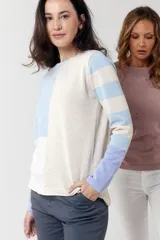 Buzo de tejido fino confeccionado en algodón, con diseño de bloques de color y rayas. Presenta un bloque azul claro en el hombro izquierdo, un bloque beige en el centro y rayas horizontales beige y azul claro en el hombro y brazo derechos. La manga izquierda es de color lila.