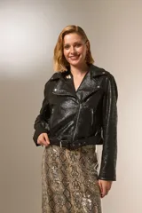 Chaqueta negra de eco-cuero con cuello solapa, cierre frontal asimétrico y cinturón ajustable. Incluye bolsillos laterales con cierre y detalles de tachas plateadas en cuello y solapa.