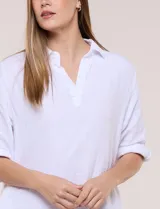 Vestido corto blanco de algodón, marca Dash, con cuello camisero, escote en V y bolsillos laterales. Presenta mangas tres cuartos y calce holgado con ruedo irregular.