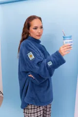 Buzo de peluche color azul, con cuello alto y diseño holgado. Presenta parches decorativos en las mangas.