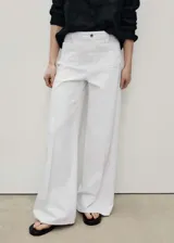 Pantalón de jean estilo wide leg, color blanco, de tiro alto con cierre frontal de cremallera y botón. Presenta dos bolsillos de parche en la parte delantera y trabillas para cinturón.