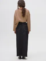 Falda midi de denim color mostaza, con tiro medio, corte recto, cierre frontal de botones metálicos y tajo delantero en el ruedo con terminación deshilachada.