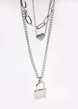 Collar de acero quirúrgico plateado con tres cadenas de diferentes largos y estilos. La cadena más corta tiene un dije de corazón negro, la más larga tiene un dije de candado plateado.