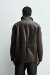 Cazadora de corte relajado confeccionada en tejido efecto piel color marrón oscuro. Presenta cuello subido con interior forrado en tejido de cuadros, manga larga, bolsillos de vivo en la cadera y cierre frontal con cremallera oculta por solapa con botones a presión.