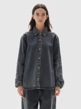 Camisa de denim de corte recto y estilo clásico, confeccionada en tejido de algodón con acabado lavado. Presenta cuello camisero, cierre frontal con botones metálicos y mangas largas con puños abotonados.